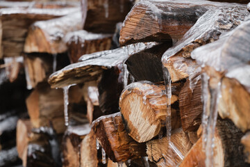 section of firewood stack covered in ice with icicles hanging from them. Aftermath of an icestorm on raw firewood