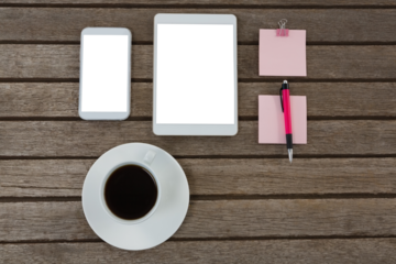 Black coffee, mobile phone, digital tablet, pen and sticky note on wooden plank
