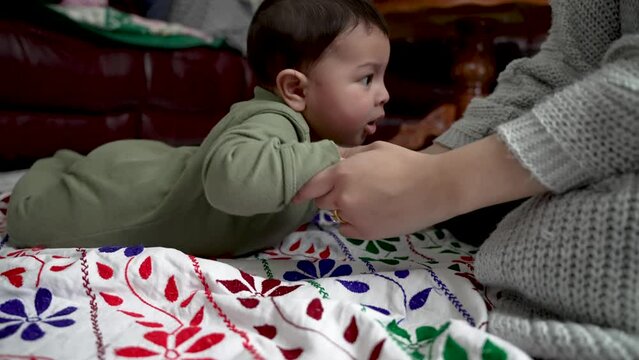 Mother Trying To Her Her Baby Son Stand Up From Lying Position On Stomach From Floor. Low Angle, Slow Motion