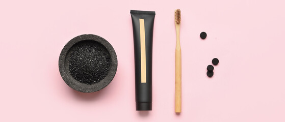 Bowl with activated charcoal tooth powder, toothpaste, bamboo brush and pills on light pink background