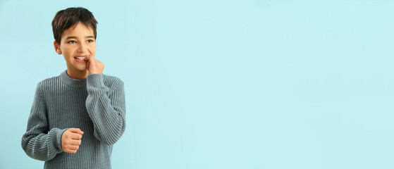 Little boy biting nails on light blue background with space for text