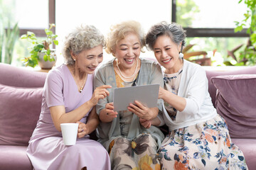 Happy senior Chinese friends using digital tablet at home