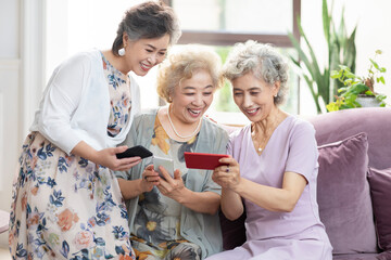 Happy senior Chinese friends using smart phones at home