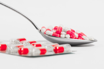 Blister and spoon with red pills on a white background. Drug overuse and antibiotic resistance.