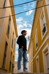 Fototapeta premium Young transgender man posing outdoors in the narrow street of a town.