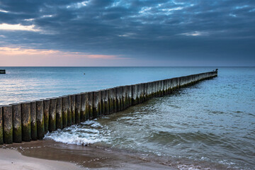 Fototapeta premium Wooden groynes on beach of Baltic sea in Svetlogorsk at sunset. Kaliningrad region. Russia