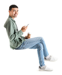 Young guy with mobile phone and cup of coffee sitting in chair on white background