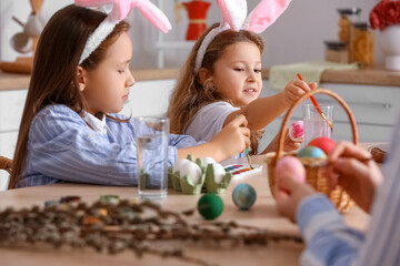 Little girls painting Easter eggs at table in kitchen