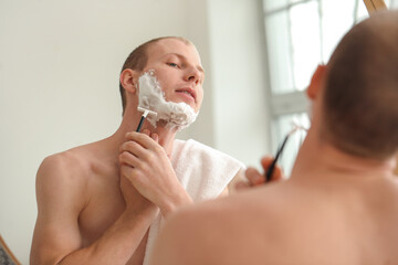Young man shaving in bathroom