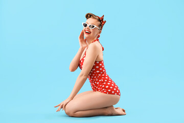 Young pin-up woman in polka dot swimsuit on blue background - obrazy, fototapety, plakaty