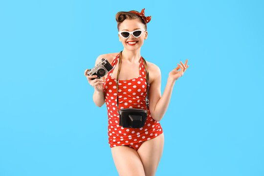 Young pin-up woman in swimsuit with photo camera on blue background