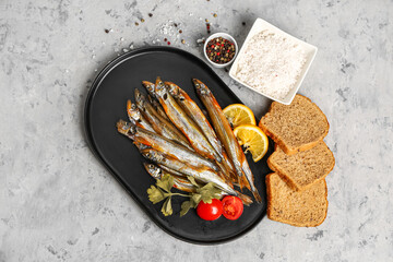 Plate with delicious smoked capelin, bread, spices and lemon on grey grunge background