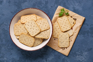 Bowl and parchment with tasty crackers on blue background