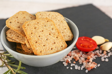 Bowl of tasty crackers, salt, tomato and garlic on slate board, closeup
