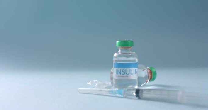 Close up of insulin vials and syringe on blue background with copy space, slow motion