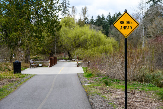 Traffic signs on a multi-use path in a public park, bridge ahead, in a peaceful garden setting
