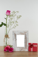 Fototapeta premium Rose flower in glass vase, photo frame and gift box