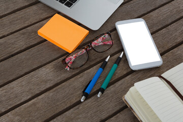 Mobile phone, laptop, pen, sticky note, spectacles and organizer on wooden plank