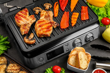 Modern electric grill with tasty steaks and vegetables on dark background
