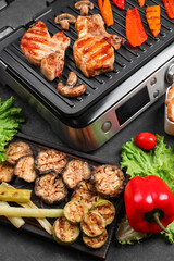 Modern electric grill with tasty steaks and vegetables on dark background