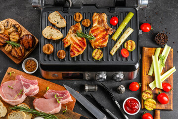 Modern electric grill with tasty steaks and vegetables on dark background