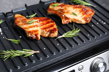 Modern electric grill with tasty steaks on dark background