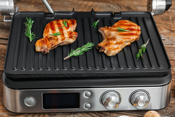Modern electric grill with delicious steaks on wooden table, closeup