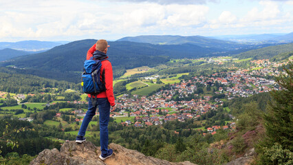 Male hiker (man) standing on mountain Silberberg and looking at panorama of municipality Bodenmais in Bavarian Forest, Germany