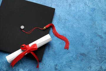 Diploma with red ribbon and graduation hat on blue table
