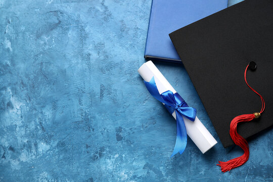 Diploma with ribbon, graduation hat and book on blue table