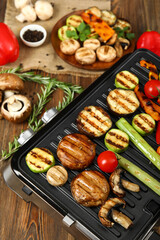 Modern electric grill with tasty vegetables on wooden background