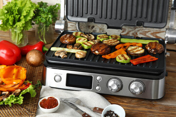 Modern electric grill with tasty vegetables on table