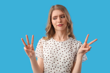 Thoughtful young woman showing fingers on blue background