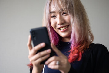 Fototapeta premium Portrait of beautiful Asian stylish trendy girl model using smartphone in casual summer clothes. pastel pink and red hair