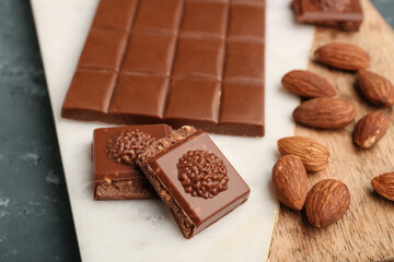 Board with tasty chocolate and almond nuts on table, closeup