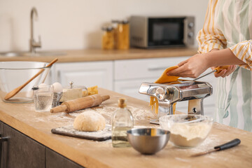 Woman making pasta with machine at table in kitchen, closeup