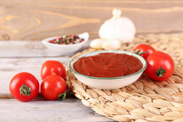 Wicker mat with bowl of tasty tomato paste on wooden background