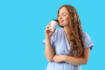 Beautiful redhead woman with cup of coffee on blue background