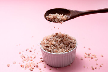 Pink Himalayan Rock Salt, Halite Pours From Wooden Spoon Over White Ceramic Bowl On Pink Background. Top View Horizontal Plane, Copy Space For Text. High quality photo