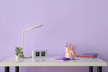 Rolgordijnen Workplace with stationery, clock and lamp near lilac wall © Pixel-Shot