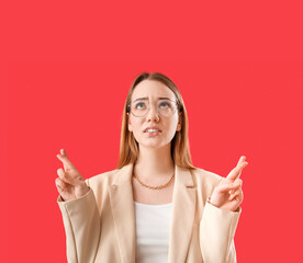 Worried young businesswoman crossing fingers on red background