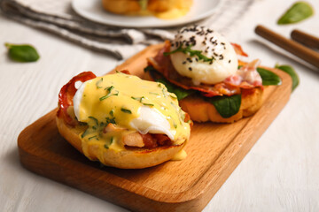 Board with delicious eggs Benedict on white wooden table, closeup