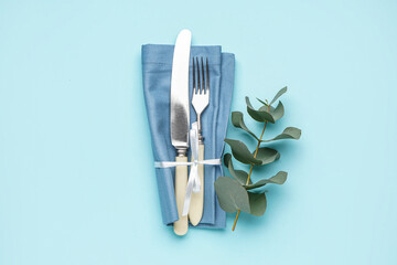 Set of cutlery in napkin and eucalyptus branch on blue background