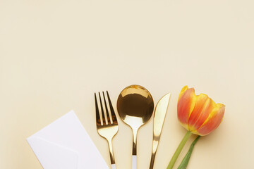 Set of cutlery, beautiful tulip flower and envelope on beige background