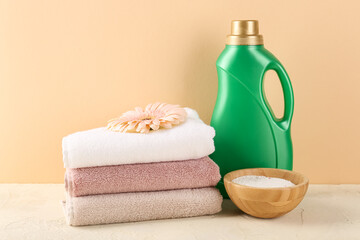 Laundry detergents, gerbera flowers and folded towels on table against beige background