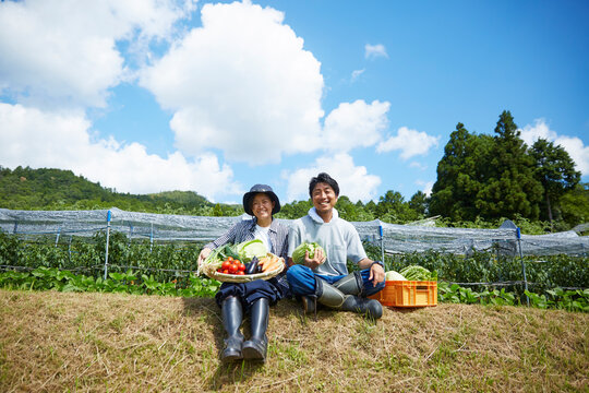 畑の前の土手に座る野菜を持つ男女