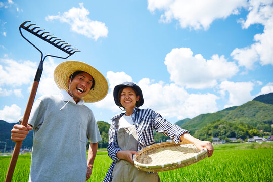 水田の前で農具をもつ男女