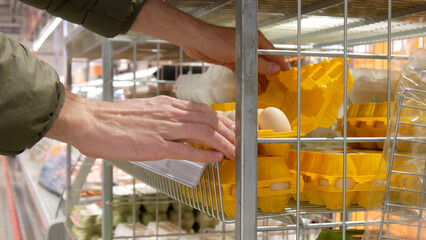 Close-up of many plastic packagings with eggs on the steel rack and two male hands open one to review