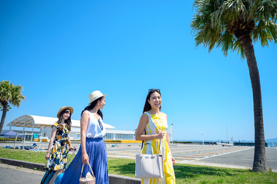 キャリーバッグを引き歩く海のリゾートへ旅する女性3人