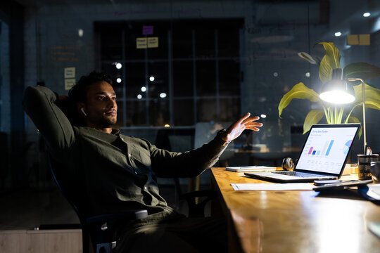 Biracial businessman sitting at desk, using laptop and working late at office